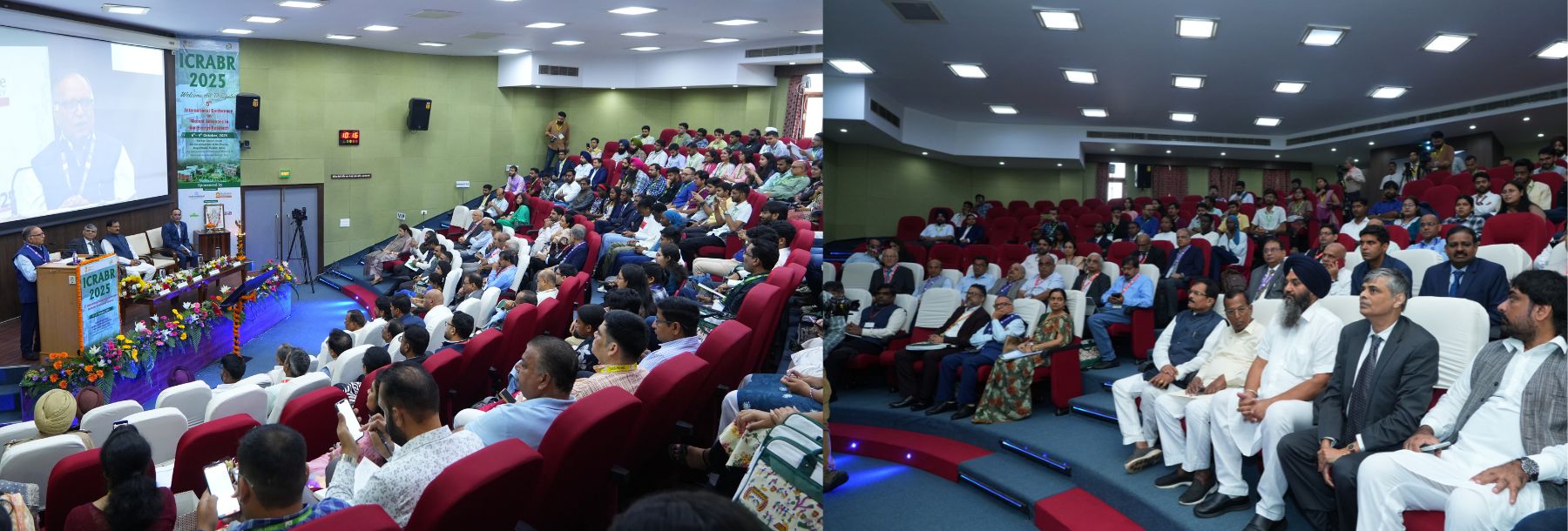 A large group of people seated in a modern auditorium attends a formal event; speakers sit at a decorated stage with flowers, banners, and a screen, while the audience listens attentively